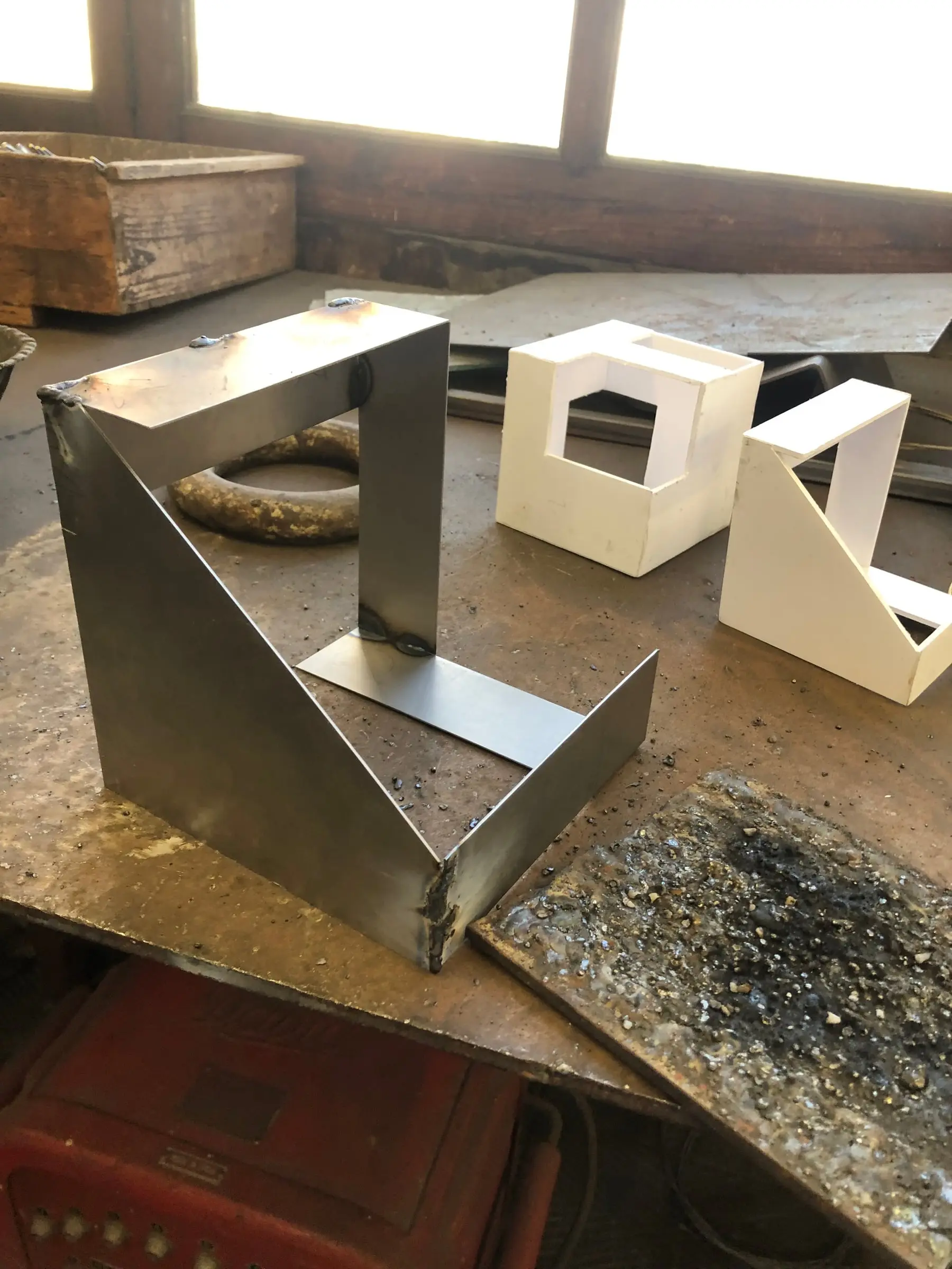 Escultura d'acer soldada al taller, devora dues maquetes blanques