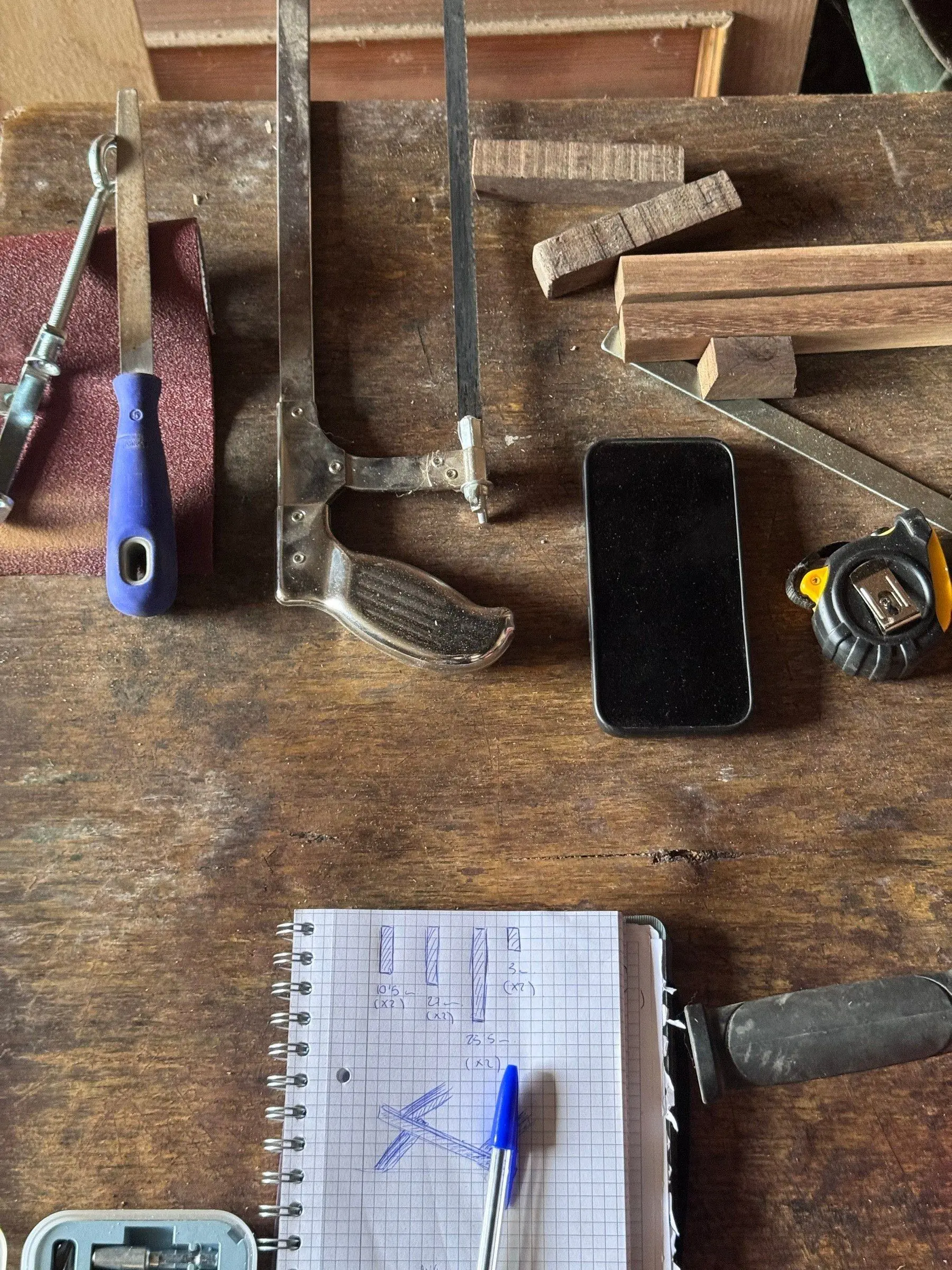 Banc de feina amb eines, fustes i una llibreta d'esbossos
